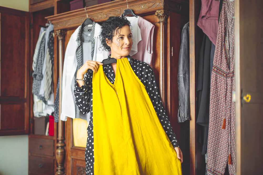 Woman deciding what to wear, holding up yellow dress in bedroom