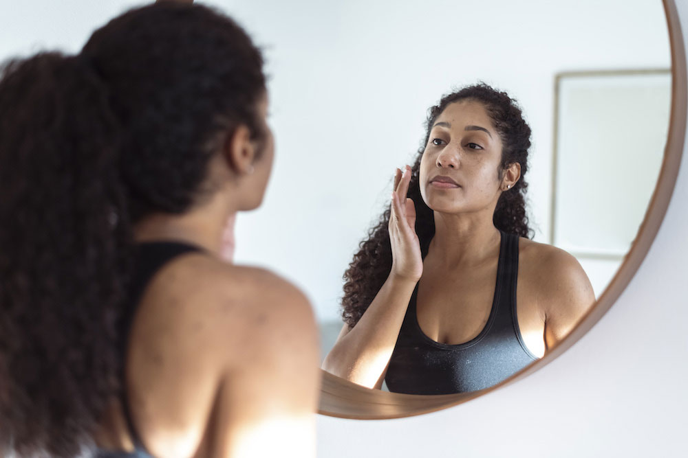 woman looking in mirror and touching her skin