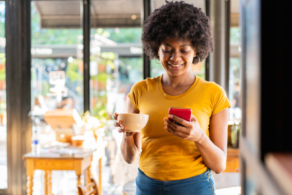 Woman holding a cup of tea in one hand and checking her phone with the other