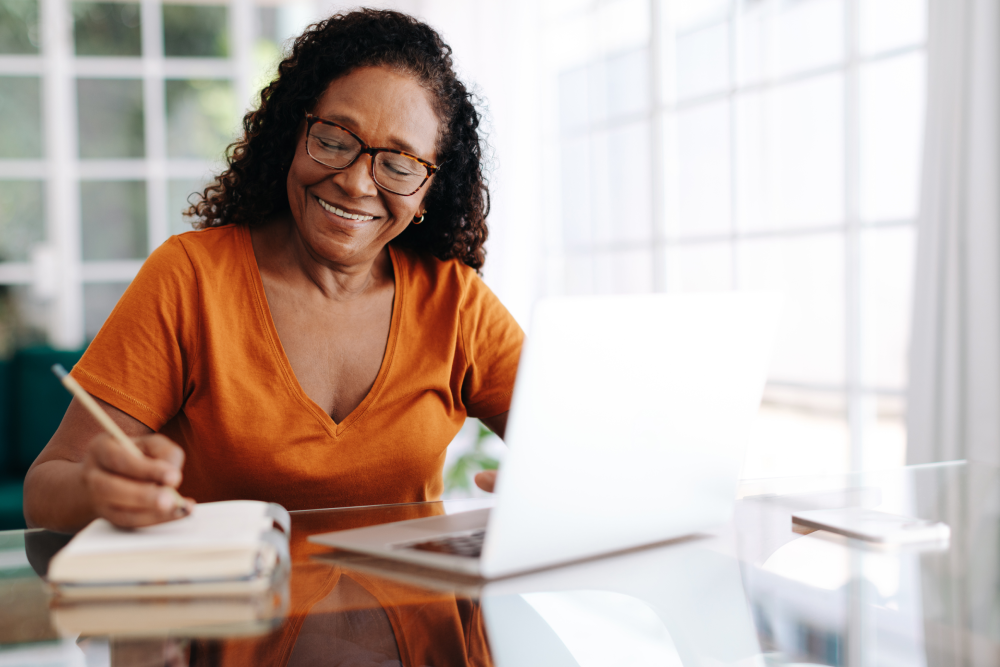 Woman writing in notebook with computer open