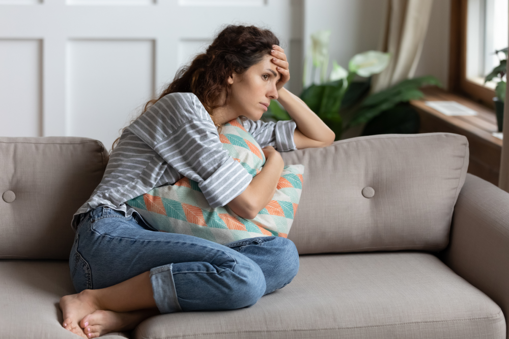 A woman sits on a couch, her head resting in her hands, conveying a sense of distress or deep contemplation